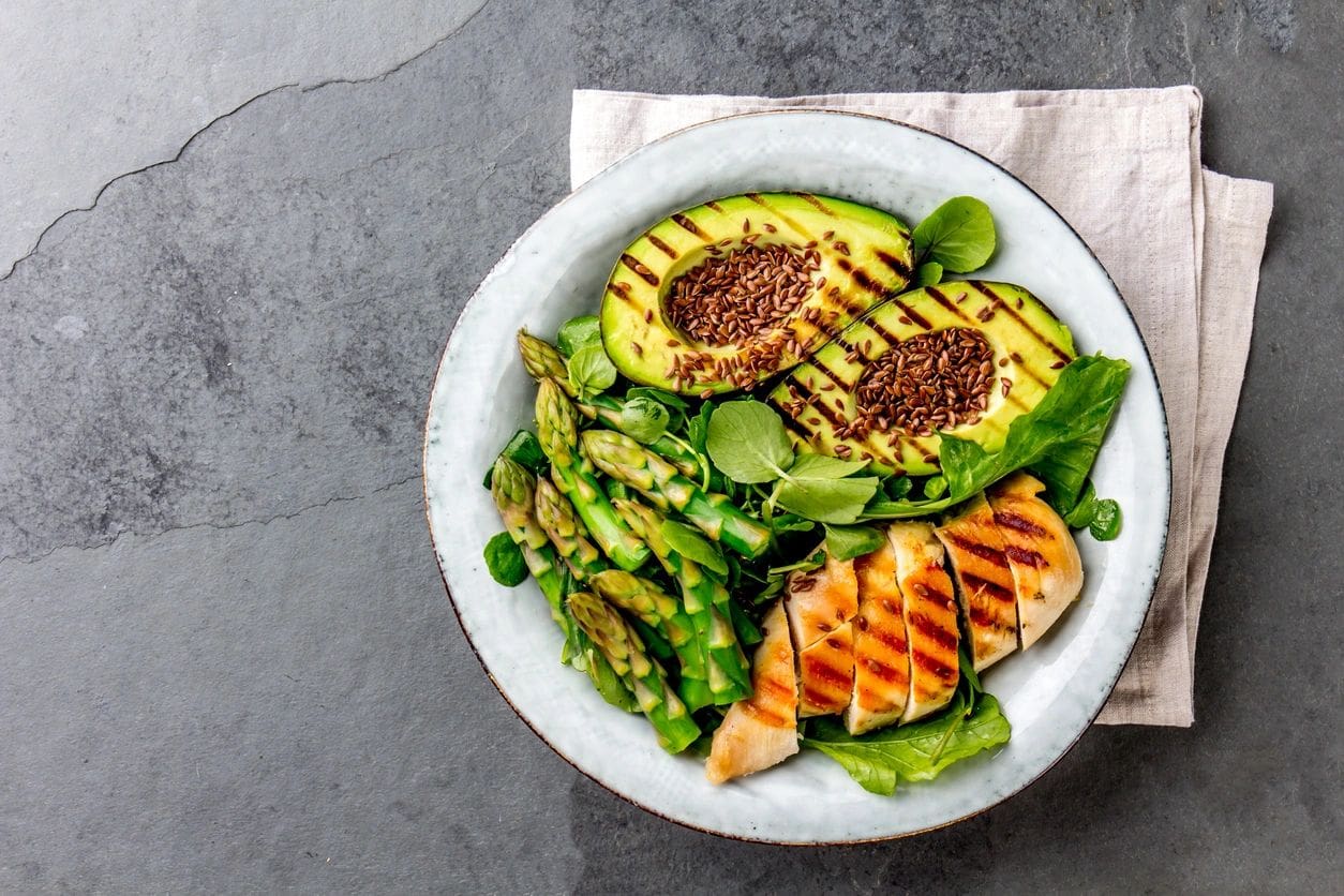 A white bowl of food with grilled chicken, asparagus and pineapple.